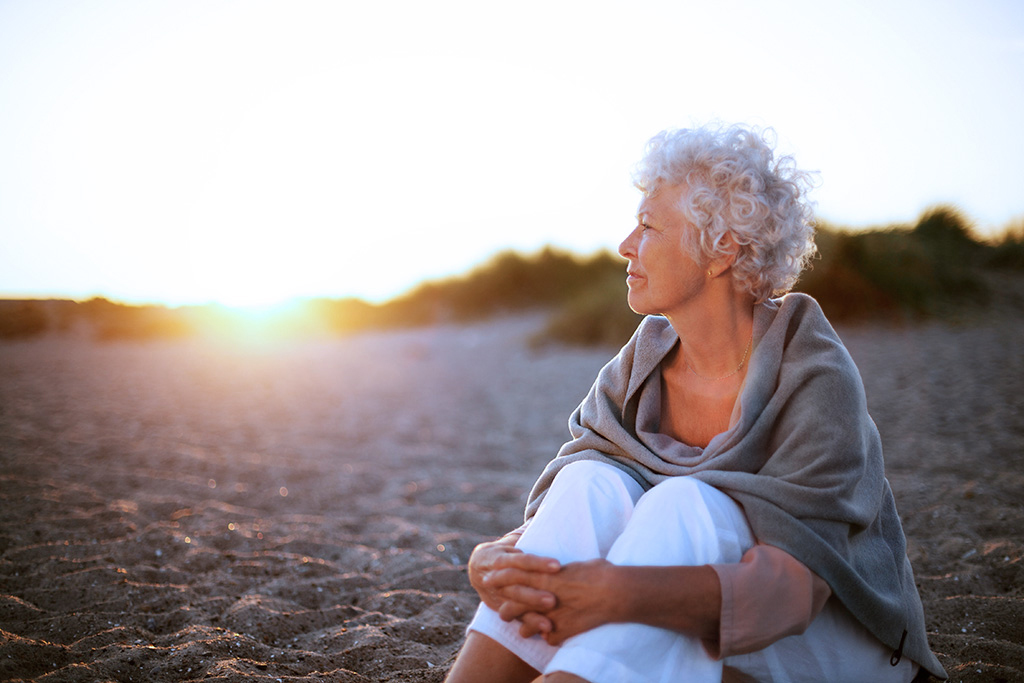Old woman sitting on the beach looking away at copyspace